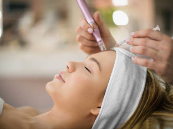 Unrecognizable beautician performs facial treatment on a young woman at beauty salon.